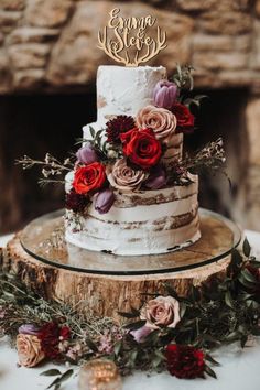 a wedding cake with flowers and greenery is on a wooden stand in front of a fireplace