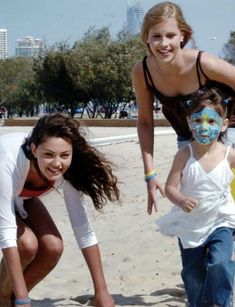 two girls and one boy are playing in the sand at the beach with their faces painted