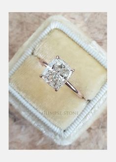 an engagement ring with a cushion cut diamond in it sitting on a velvet box,