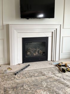 a flat screen tv mounted above a fireplace in a living room with tools on the floor