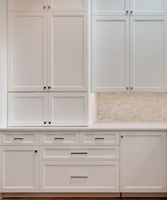 a kitchen with white cabinets and marble counter tops