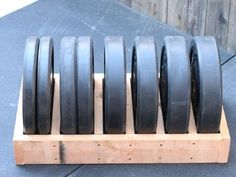 several black tires are lined up in a wooden holder on top of the pavement outside