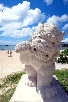 a stone lion statue sitting on top of a cement slab next to the ocean with people in the background