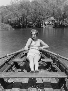 a woman sitting in the bow of a boat on a lake with her legs crossed