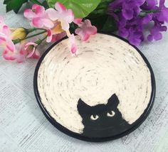 a black and white plate with a cat's face on it next to purple flowers