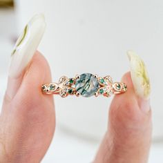 Inspired by nature's delicate beauty, the Moss Blossom ring features a round-cut natural moss agate as the centerpiece, symbolizing the serene connection between earth and art. The band is adorned with petal-like designs on each side, reminiscent of a blooming flower cradling a vibrant green fruit. Each petal is embellished with moissanite, adding a subtle sparkle that enhances the ring’s organic charm. The design seamlessly blends natural inspiration with elegance, perfect for those who appreciate understated sophistication in everyday wear. 𝗗𝗘𝗧𝗔𝗜𝗟𝗦𝗠𝗔𝗜𝗡 𝗦𝗧𝗢𝗡𝗘𝗚𝗲𝗺𝘀𝘁𝗼𝗻𝗲: Natural Moss Agate𝗖𝗼𝗹𝗼𝗿: Green𝗦𝗵𝗮𝗽𝗲: Round 5mm𝗖𝘂𝘁: Full𝗠𝗲𝗮𝘀𝘂𝗿𝗲𝗺𝗲𝗻𝘁: 1.0 ct approx𝗤𝘂𝗮𝗹𝗶𝘁𝘆: VS clarity grademoss agate are natural and can therefore slightly vary in color Natural Inspiration, Rutilated Quartz Ring, Art Ring, Moss Agate Ring, Engagement Rings Bridal Sets, Gothic Rings, Rose Quartz Ring, Textured Ring, Black Onyx Ring