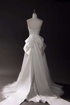 a white wedding dress on display in front of a black background with an open back