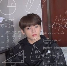 a young man is sitting in front of a blackboard with numbers and calculations on it