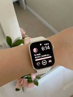 a woman's arm with an apple watch displaying the time on her wrist and pink flowers in the background