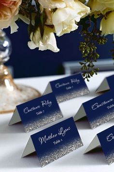 place cards are placed on a table with flowers in the vases behind them for seating