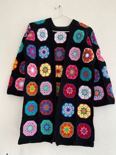 a black crocheted sweater with multicolored flowers on it hanging from a hook