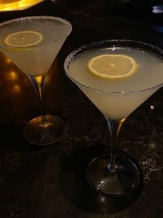 two martinis with lemon wedges on the rim sit on a bar top, ready to be served