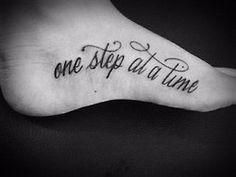 a foot with the words one step at a time written on it in cursive font