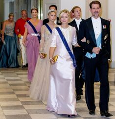 a group of people in formal wear walking down a hall with other people behind them