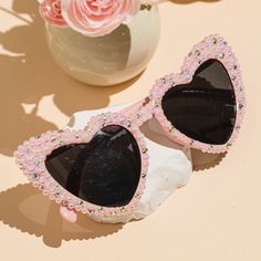 a pair of heart shaped sunglasses sitting on top of a table next to a vase with flowers