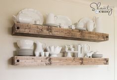 two wooden shelves filled with white dishes and cups on top of each other in front of a wall