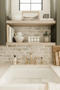 a white sink sitting under a window next to a shelf filled with books and other items