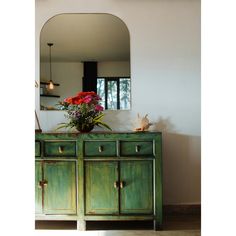 a green dresser with flowers on top and a mirror in the corner behind it,