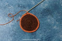 an orange crocheted potholder with a hook on the end, sitting on a blue surface