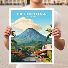 a man holding up a poster with a mountain in the background that reads la fortuna costa rica