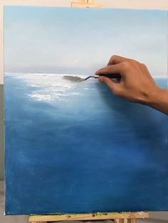 a person is painting an ocean scene with blue water