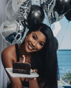 a woman holding a plate with a piece of cake on it in front of balloons