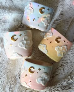 four ceramic cups with clouds and stars on them sitting on a white blanket in the shape of hearts