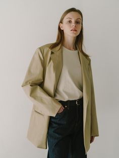 The individual is wearing an oversized blazer with a notched lapel, a contemporary take on classic suiting. The blazer has a single-button closure, which creates a streamlined and modern look. Its length extends to mid-thigh, offering a relaxed and stylish silhouette that could easily transition from office wear to casual settings. The fabric seems to have a smooth texture and a slight sheen, suggesting a blend that may include materials like viscose or silk.- The oversized fit is a nod to current trends, providing a comfortable yet chic aesthetic.- The neutral tone of the blazer makes it a versatile piece for layering over different outfits.- The simplicity of the design, with minimal visible detailing, gives this blazer a clean and sophisticated finish. Chic Aesthetic, Blazer Beige, Current Trends, Oversized Blazer, Different Outfits, Leather Blazer, Office Wear, Smooth Texture, Layering