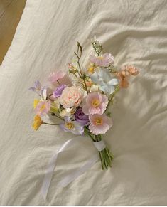 a bouquet of flowers laying on top of a white bed sheet with a ribbon tied around it