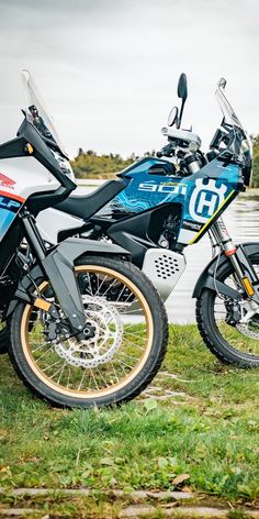 two motorcycles parked next to each other in the grass near a body of water on a cloudy day