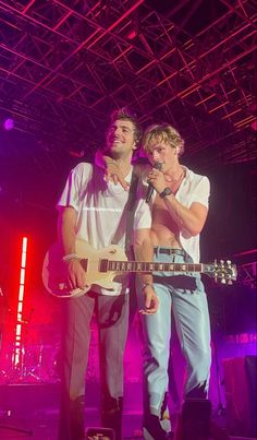 two young men singing into microphones on stage