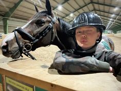 a young boy wearing a helmet leaning on a fence next to a horse