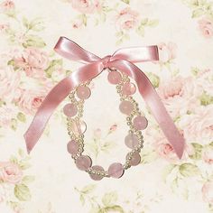 a pink ribbon and some beads on a flowered wall with roses in the background