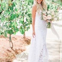 a beautiful blonde woman in a white dress holding a bouquet and smiling at the camera