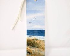 a bookmark with a watercolor painting of birds flying over the ocean and sand dunes