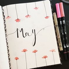 an open notebook with the word may written on it next to some markers and pens