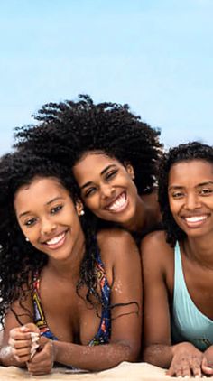 three beautiful young women laying on top of a beach next to the ocean, smiling at the camera