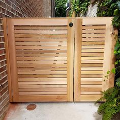 two wooden gates are open in front of a brick wall and green plants on the sidewalk