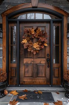 a wooden door with a wreath on it and autumn leaves in the foreground next to it