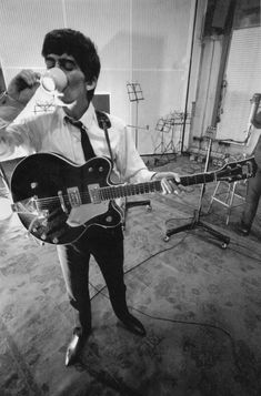 a man in a suit and tie drinking from a cup while playing an electric guitar