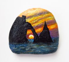 a painted rock sitting on top of a white surface with the sun setting behind it