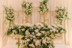 an arrangement of white flowers and greenery in front of a gold frame on a bed