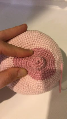 a hand is holding a pink and white knitted object on a counter top,