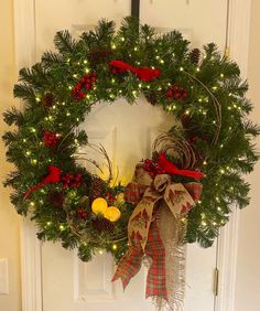 a christmas wreath hanging on the front door with lights and ribbons around it, decorated with pine cones, holly leaves, red berries, and oranges