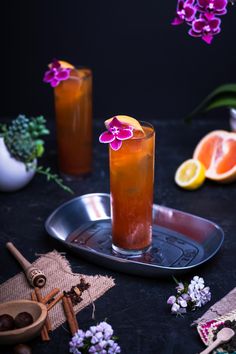 two glasses filled with orange juice and garnished with purple flowers on a tray