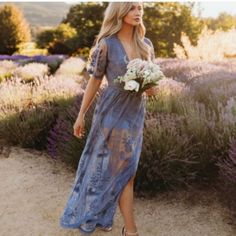 a woman in a blue dress is walking through lavender fields with flowers and holding a bouquet