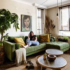 a woman sitting on top of a green couch in a living room next to a potted plant