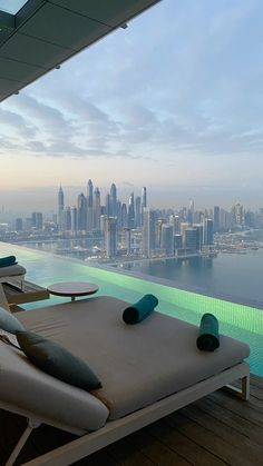 two lounge chairs sitting on top of a wooden deck next to a swimming pool with the city in the background