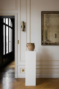 a vase sitting on top of a white pedestal in front of a painting hanging on the wall