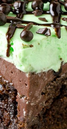 a piece of chocolate cake with green frosting and chocolate chips on top, sitting on a plate